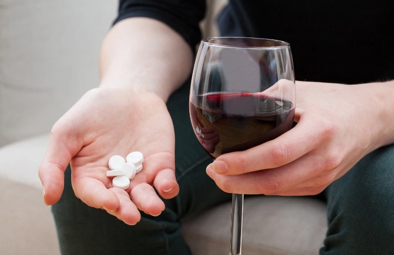 osoba trzymająca tabletki i kieliszek wina